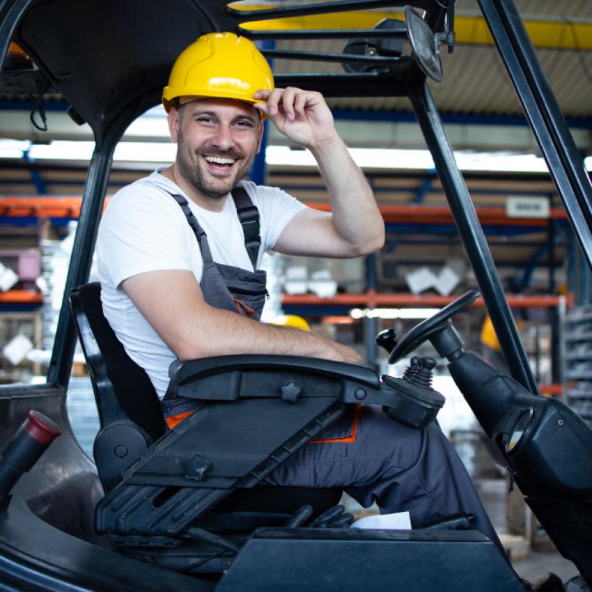 Cariste avec un casque qui conduit une machine dans un entrepôt.